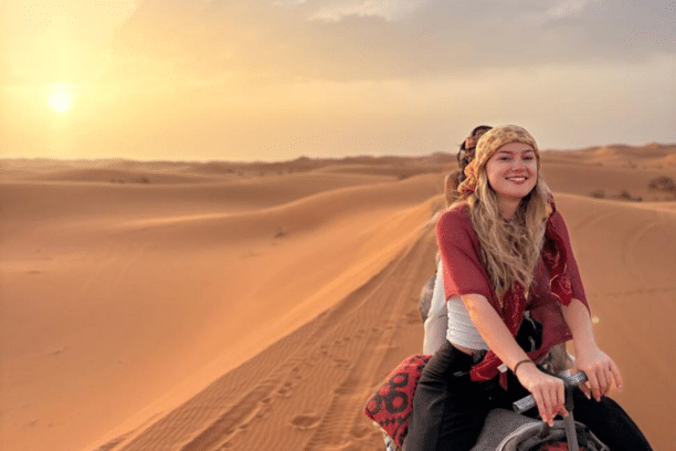 Traveler riding a camel across the golden dunes of the Merzouga Sahara Desert during a sunset Morocco desert tour.